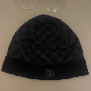 Louis vuitton mössa Navy blue - Snygg svart mössa från Louis Vuitton med klassiskt rutigt mönster och LV-logga framtill. Mjuk och varm, perfekt för kyliga dagar. Stilren design som lyfter din outfit. Navy edition Limited mitt pris 2000kr sällsynt 