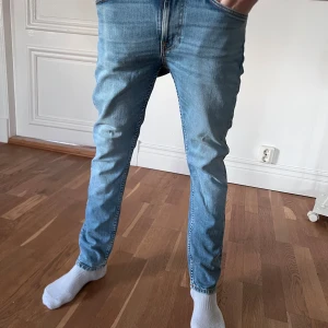  Nudie Jeans - Säljer ett par ljusblå jeans från Nudie Jeans i storlek 28/28. Jeansen har klassisk femficksdesign, orangea sömmar och Nudie Jeans signaturbroderi på bakfickorna. Modellen är rak med normal passform och tillverkad i bomull.