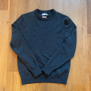 Mörkgrå merinoulltröja These Glory Days - Snygg mörkgrå stickad tröja från These Glory Days i mjuk och lyxig merinoull. Klassisk rund hals och långa ärmar, perfekt för dig som gillar stilrena och bekväma plagg. Passar dig som vill ha en enkel men schysst look. Krymt lite i tvätten så mer som S.