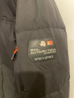 Svart pufferjacka från Sail Racing - Svart pufferjacka från Sail Racing med Sail Antarctica Expedition patch. Storlek M. Jackan är i använt skick men fortfarande bra skick. 