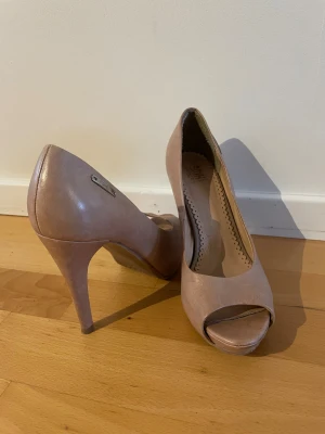 Beiga pumps med öppen tå - Beiga pumps med hög klack och öppen tå. Skorna har en rundad form och är tillverkade i skinn. 