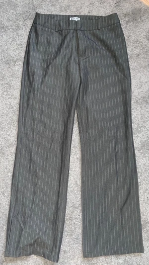 Grå randiga kostymbyxor från Madlady - Helt oanvända grå kostymbyxor från Madlady med smala vita ränder. Byxorna har hög midja, raka ben och klassisk stängning med dragkedja och hyska. Materialet är mjukt och har en lätt stretch för skön passform. Perfekt för dig som gillar stilrena och trendiga byxor.
