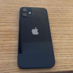 iPhone 12 - Snygg svart iPhone 12 med dubbla bakre kameror. Telefonen ser ut att vara i gott skick utan synliga sprickor eller större repor på skärm eller baksida. Perfekt för dig som vill ha en kraftfull och stilren smartphone.