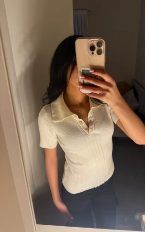 Beige elegant tröja  - Säljer en vit ribbad polotopp med korta ärmar och snygg krage. Toppen har tre knappar framtill och är figurnära i modellen. Perfekt för dig som gillar stilrena och klassiska plagg med en modern twist.