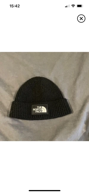 Svart ribbad mössa från The North Face - Svart ribbstickad mössa från The North Face med uppvikt kant och tydlig logotyp framtill. Klassisk och enkel design som passar till allt. Tillverkad i mjukt och stretchigt material för skön passform.