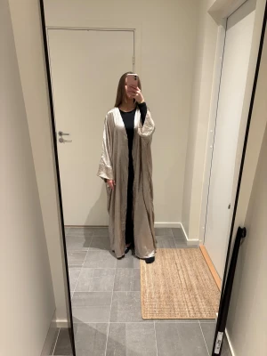 Open Abaya - Sälker min open abaya, den är skimrig i typ champagne färg, lite ljusare än vanlig champagne färg skulle jag säga. Jag är 166 cm lång, aldrig använd och har inga defekter. 