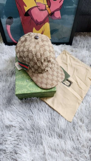 Keps med GG-mönster - Snygg beige keps i med klassiskt GG-monogram över hela kepsen. Har en grön och röd rand på sidan och justerbar rem baktill. Materialet är bomull och insidan är brun. Perfekt för dig som vill ha en lyxig och trendig accessoar.