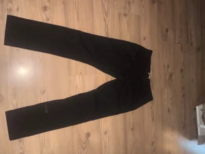 Svarta slim fit kostymbyxor från !SOLD - Svarta kostymbyxor från !SOLD i slim fit-modell. Byxorna har rak siluett och klassisk design med diskret midja. Materialet är mjukt och följsamt, perfekt för dig som gillar stilrena och enkla plagg. Passar dig som vill ha en clean look.