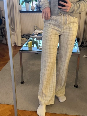 Beige-rutiga wide byxor från NA-KD - Säljer ett par beige och vita rutiga byxor från NA-KD i storlek 38. Byxorna har breda ben, hög midja med snörning, riktigt luftiganoch sköna.