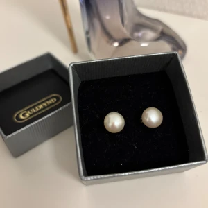 Örhängen i äkta silver med odlade sötvattenspärlor från Guldfynd - Örhängen i äkta silver med odlade sötvattenspärlor från Guldfynd i vit färg och silver. Örhängena har rund form och kommer i originalask. Perfekta för dig som gillar stilrena och tidlösa smycken med en elegant touch.