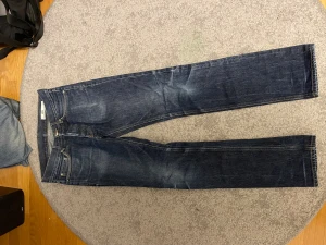 Mörkblå jeans från HOPE, straight fit - Snygga mörkblå jeans från HOPE med klassisk femficksdesign och raka ben. Jeansen har subtila slitningar och kontrastsömmar, vilket ger en cool och tidlös look. Passar dig som gillar stilrena och enkla jeans med lite edge.