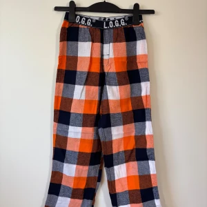 L.O.G.G. Mjukisbyxor - 146/152 Storlek - Mjukisbyxor från H&M L.O.G.G. i storlek 146/152 med stort rutmönster i orange, marinblå, grå och vit. Byxorna har elastisk midja med och är tillverkade i mjukt bomullsmaterial.