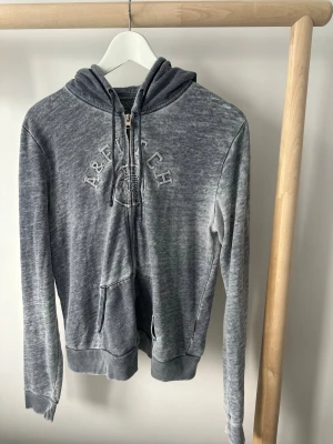 Grå hoodie Abercrombie & Fitch - Grå hoodie från Abercrombie & Fitch i storlek L. Tröjan har dragkedja, huva med snörning och broderad logga på bröstet. Mjuk bomullskänsla. Distressed stil. Passar som storlek M.