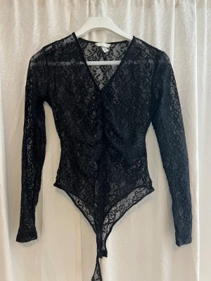 Svart spetsig långärmad blus - Säljer en svart långärmad blus i transparent spets med blommigt mönster och v-ringning. Den är från H&M och är i storlek S. 
