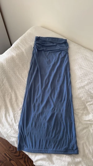 Blå långkjol och topo  med drapering - Snygg blå långkjol och topp med draperad midja och mjukt, stretchigt material. Kjolen har en enkel design utan mönster och sitter tight över höfterna. Perfekt för dig som gillar stilrena plagg med lite extra detalj vid midjan.