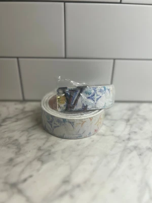 Bälte - Vitt bälte med färgglatt mönster  Helt nytt och aldrig använt! 🤍 Fint vitt bälte med färgstarkt, lekfullt mönster och silverfärgat spänne (plastskyddet sitter kvar). En accessoar som verkligen sticker ut 🌈 📦 Snabb och säker leverans! 