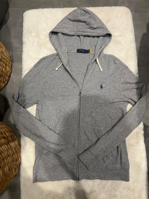 Grå hoodie från Ralph Lauren - Snygg grå zip hoodie från Ralph Lauren. Mycket bra skick. Inga defekter, nästan som ny. Storlek S
