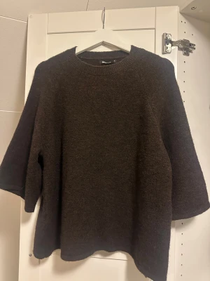 Mörkbrun stickad tröja med trekvartsärm - Mysig mörkbrun stickad tröja från Gina med rund hals och trekvartsärmar. Tröjan har en loose passform och är perfekt för lager-på-lager under kyliga dagar. Materialet är mjukt och ger en avslappnad vibe.