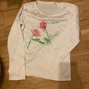 Vit långärmad tröja med rosor - Säljer en vit långärmad tröja med tryck av två rosa rosor och gröna blad på framsidan. Tröjan är nästan som fleece material. Ingen strl står. 