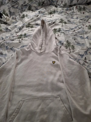 Vit hoodie från Lyle & Scott Junior - Vit hoodie från Lyle & Scott Junior med klassisk gul broderad örn på bröstet. Tröjan har huva, lång ärml. Mjuk och skön bommullsmartial Snygg och enkel design som funkar till det mesta. Storlek s 