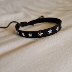 Svart armband med silverstjärnor - Coolt svart armband med justerbar knytning och silverfärgade stjärnor längs hela bandet. Armbandet har en mjuk yta och passar perfekt för dig som gillar detaljer med lite edge. Armbandet är aldrig använt men det fungerar bara att justera med ena bandet. Men det går att justera till den minsta storleken och mycket större.