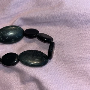 Svart armband med ovala stenar - Snyggt armband med stora, ovala svarta stenar i glansig finish. Stenarna är trätt på elastisk tråd och har en cool, naturlig look med lite marmorerad känsla. Perfekt accessoar för att lyfta din outfit med en stilren touch.