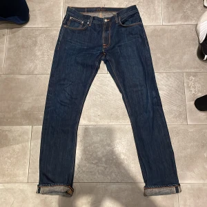 Nudie Jeans Selvedge  - Snygga blå selvedgejeans från Nudie Jeans, modell Thin Finn. Jeansen är tillverkade i 100% ekologisk bomull och har klassiska orange sömmar samt smal passform. Fina detaljer med vikta benslut och broderade bakfickor. Storlek är 34 36 men sitter mer som 33 34.
