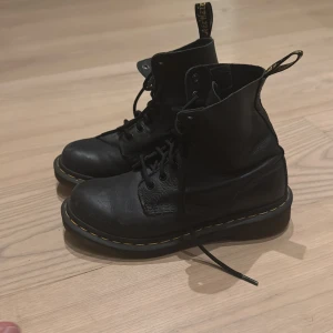 Svarta Dr.martens 1460 Pascal  - Superfina klassiska svarta boots i mjukt skinn med snörning och den ikoniska gula sömmen runt sulan. Rund tå och platt sula, perfekt för dig som vill ha en tidlös och edgy stil. Dragflik baktill med Dr. Martens-logga. Nypris 2100kr