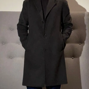 Mörkgrå rock från Bläck i ull, stl 46 - Stilren mörkgrå rock från Bläck i klassisk modell med krage och knäppning framtill. Jackan är tillverkad i ull och har två fickor på sidorna. Perfekt för dig som vill ha en clean och tidlös look under höst och vinter. Rocken är i väldigt bra skick. Modell: 180 cm, 72 kg. Kontakta gärna vid fler frågor!