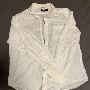 Vit klassisk skjorta från Nautica - Vit skjorta från Nautica i klassisk passform, tillverkad i mjuk bomull. Skjortan har långa ärmar, krage och knappar framtill samt diskret logodetalj vid nederkanten. Perfekt för en clean och stilren look. Storleken är XL och skick är 7/10, vid mer information kontakt vänligen mig!