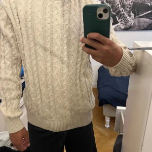 Beige kabelstickad tröja från Kappahl - Säljer en beige kabelstickad tröja från Kappahl i storlek 146/152. Tröjan har ett klassiskt flätmönster, ribbade muddar vid ärmslut och nederkant samt rund hals. Aldrig använd!!. Jag på bilden är 160cm och den passar fortfarande mog. DEN ÄR STOR I STORLEKEN!!