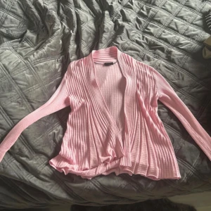 Ljusrosa ribbad kofta från Freequent - Säljer en ljusrosa, ribbad kofta från Freequent i storlek S. Koftan har öppen front, långärmad design och är tillverkad i mjukt, stretchigt material som känns skönt mot huden. Perfekt för lager-på-lager och chill dagar.