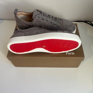 Grå mocka sneakers från Louboutin - Snygga grå sneakers från Christian Louboutin i mjuk mocka med klassisk snörning och rund tå. Med skorna följer tre dustbags till. Skorna har en vit sula med den ikoniska röda undersidan och subtila Louboutin-logga. Perfekt för dig som vill ha en exklusiv och stilren look. Priset kan sänkas vid snabb affär!!