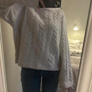 Vit stickad kabeltröja - Mysig vit stickad tröja med kabelstickat mönster och långa ärmar. Tröjan har en loose passform och bred ribbad kant nedtill och vid ärmsluten. Perfekt för kyliga dagar och enkel att matcha med jeans eller kjol.