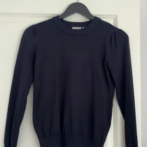 Svart tröja från Saint Tropez XS - En svart, klassisk tröja från Saint Tropez i storlek XS. Tröjan har rund halsringning med bred ribbad kant och långa ärmar med lätt puff vid axlarna. Perfekt basplagg till garderoben och enkel att styla med olika outfits.