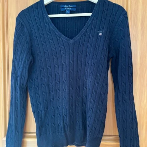 Mörkblå kabelstickad tröja GANT - Kabelstickad mörkblå tröja från GANT med v-ringning och logga på bröstet 💕 köpt second hand men i nyskick!! Säljer billigt ❤️