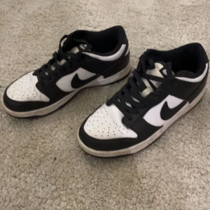 Nike Dunk Low svartvita sneakers - Svartvita Nike Dunk Low sneakers med klassisk design. Skorna har svart swoosh, svart snörning och perforerad vit tå. Lågt skaft och platt sula, perfekt för dig som gillar streetwear och vill ha en stilren look. Materialet är syntet och skinn.