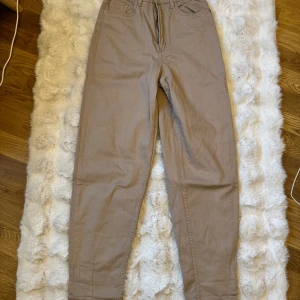 Beiga/bruna high waist byxor från H&M - Snygga beiga/bruna byxor från H&M med hög midja och raka ben. Byxorna har klassisk femficksdesign, bälteshällor och dragkedja med knapp. Tillverkade i bomull för en skön känsla och stilren look.
