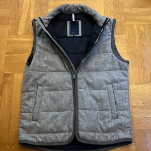 	Exklusiv Berkeley väst i italiensk ullflanell, Medium - Snygg och stilren grå quiltad väst från Berkeley i samarbete med exklusiva Vitale Barberis Canonico. Tillverkad i italiensk ullflanell och helfodrad för en elegant och bekväm känsla.  Passar perfekt både över skjorta, stickad tröja eller kavaj – en mångsidig klassiker för både vardag och mer uppklädda tillfällen.  Storlek Medium. Skick 10/10 – som ny. Nypris ca 2500 kr, säljes för 1200 kr. 