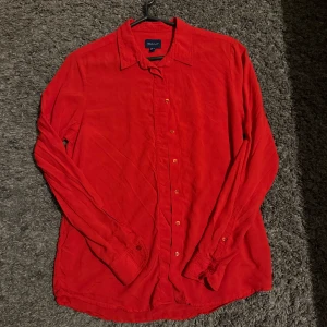 Röd skjorta från GANT  - Riktigt snygg röd skjorta från GANT med klassisk krage och knappar hela vägen. Skjortan är långärmad och har broderad GANT-logga vid manschetten. Tillverkad i mjuk bomull som känns skön mot huden.