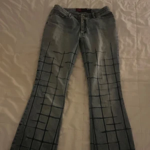 Low Rise ljusblå jeans med mörka detaljer - Unika ljusblå jeans från Yunique Jeans med mörkblått rutigt mönster över hela benen och bakfickorna. De är lågmidjade och flare i modellen. De har lite slitningar längst ner på benen. Det är bara att fråga om fler bilder eller mått! Jag är öppen för prisförslag!