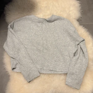 Grå ribbad tröja från H&M - Mysig ljusgrå ribbad tröja från H&M med lång ärm och rak passform. Tröjan är tillverkad i ett mjukt material och har en enkel, stilren look som passar perfekt till jeans eller kjol.