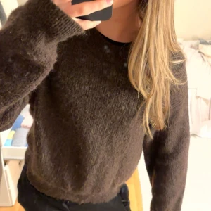 Brun stickad tröja från Lindex - Mysig brun stickad tröja från Lindex med rund halsringning och ribbade muddar. Tröjan har en loose passform och långa ärmar, perfekt för lager-på-lager under kyliga dagar. Enkel och stilren design som funkar till allt.