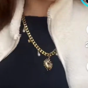 Guldfärgat halsband med pärldroppar - Snyggt guldfärgat halsband med chunky kedja, dekorerat med vita pärldroppar och ett stort solformat hänge i mitten. Perfekt statement-piece som lyfter vilken outfit som helst. Passar dig som gillar unika detaljer och trendig stil.