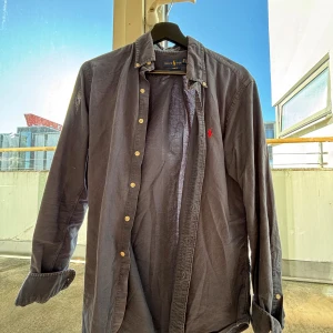 Ralph Lauren skjorta - Säljer en mörkblå skjorta från Ralph Lauren i slim fit-modell. Skjortan har klassisk krage, knappar framtill och den ikoniska röda broderade loggan på bröstet. Tillverkad i 100% bomull och har långa ärmar. Perfekt för en clean och stilren look. Skjortan är använd men har inga tecken på defekter! Pris går att diskutera.
