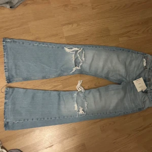 Ljusblå flare jeans från Pull&Bear - Säljer ett par ljusblå flare jeans från Pull&Bear i storlek 38. Jeansen har slitna detaljer och hål på benen för en trendig look. Klassisk femficksmodell med dragkedja och knapp. Perfekta för dig som gillar en avslappnad och cool stil.