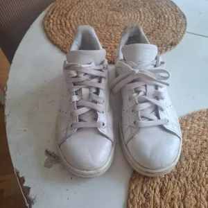 Adidas Stan Smith vita sneakers 36⅔ - Klassiska vita Adidas Stan Smith sneakers med snörning och perforerade detaljer på sidorna. Skorna har rund tå, platt sula och är tillverkade i skinn. Perfekta för en clean och tidlös stil.