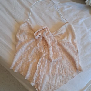 Ljusrosa spets tubtopp med rosett - Säljer en ljusrosa tubtopp i spets med snygg rosettdetalj framtill och smal halterneck-rem. Toppen har ett spetsmönster och är fodrad på insidan. Perfekt för dig som vill ha en feminin och trendig look.