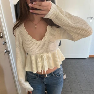 Vit stickad topp - Supersöt vit stickad topp med lång ärm, volangkant vid halsringningen och knytband i midjan. Croppad modell med peplum-effekt❣️