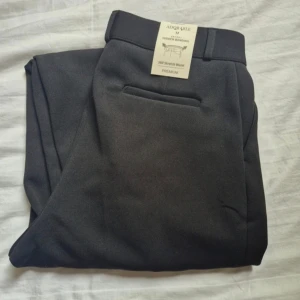 Svarta kostymbyxor med stretch - Svarta kostymbyxor från Lewkin(koreanskt märke)med stretchig midja och klassisk rak passform. Materialet är mjukt, bekvämt och skrynkelfritt, perfekt för dig som vill ha en clean look. Byxorna har bälteshällor och diskret bakficka. Snygga till skjorta eller t-shirt. Jag är 167 och ben längden e perfekt! Alla etiketter kvar  Orginal pris 465 kr